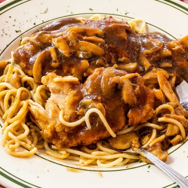 Chicken and mushroom marsala with spaghetti on a white plate with green stripes, on a red and white checkered tablecloth.