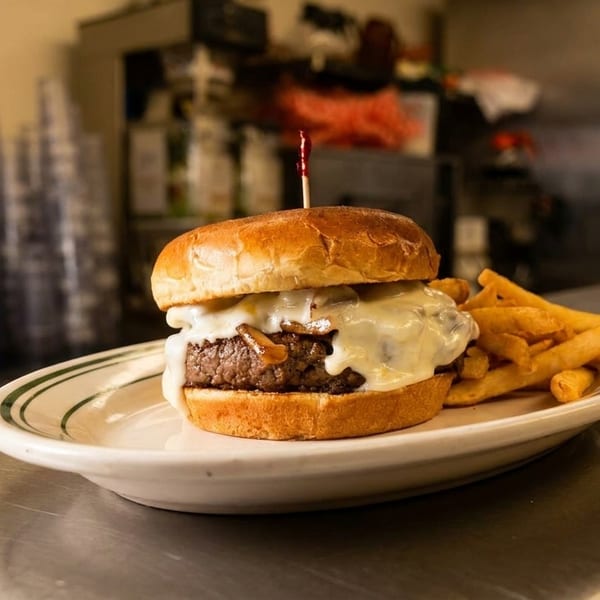 Cheeseburger with sautéed onions and fries on a diner counter, with kitchen equipment in the background.